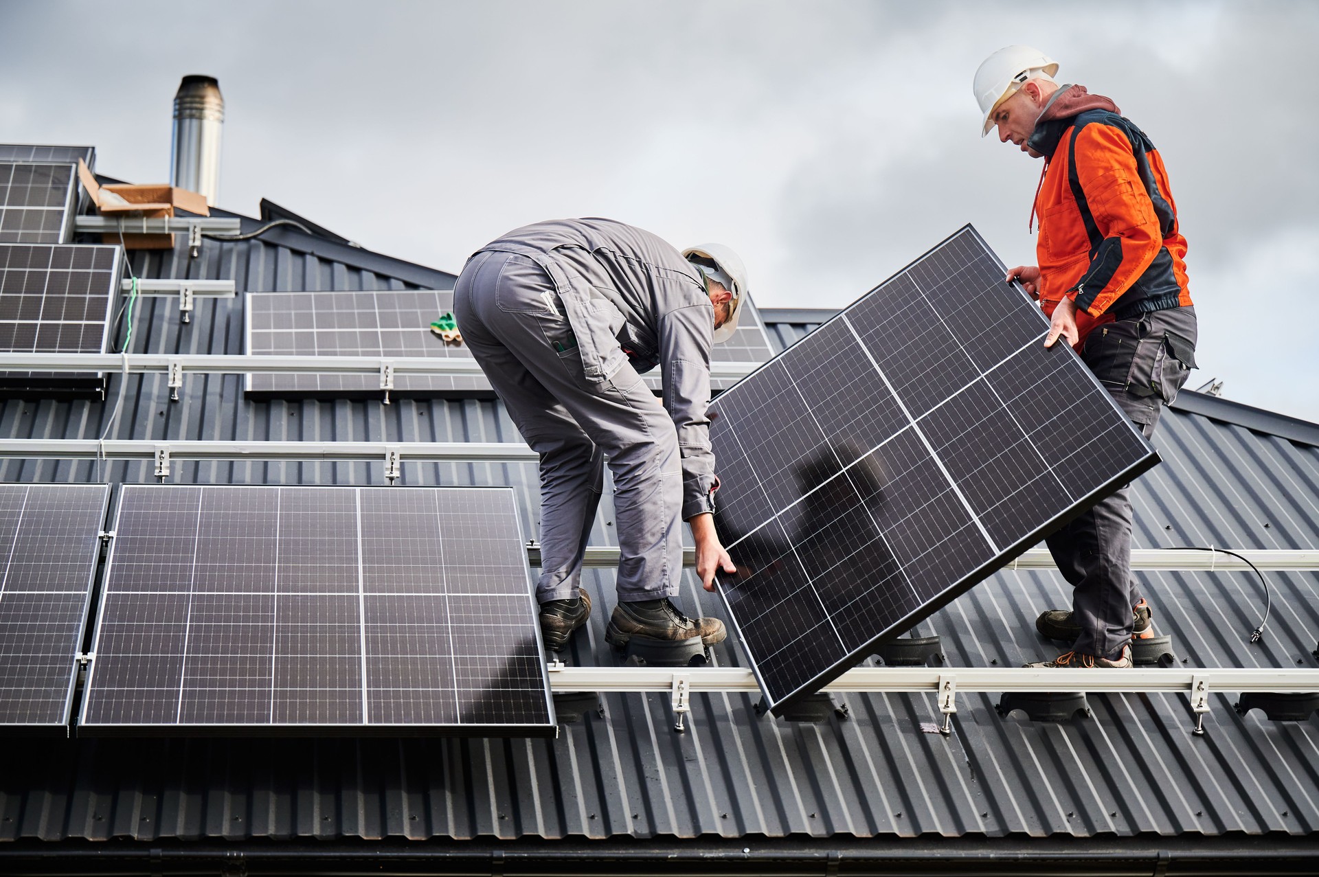 Technicians carrying photovoltaic solar module while installing solar panel system on roof of house